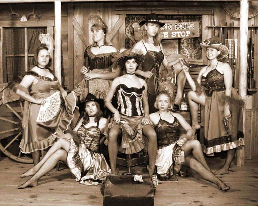 Seven women in vintage western costumes posing inside a rustic saloon. — Old Picture