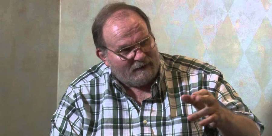 An older man with glasses and a beard gestures while speaking indoors. — Ole Anderson Wallpaper