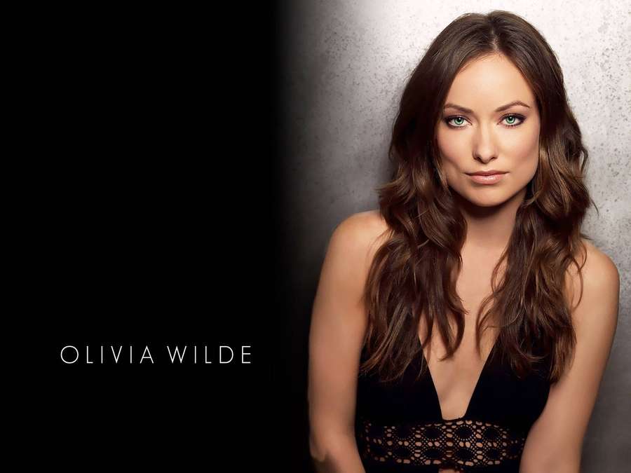 Olivia Wilde in a black lace top against a gray wall with text overlay. — Olivia Wilde Wallpaper