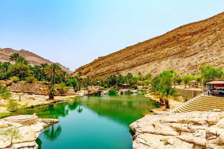 Oasis with turquoise water and palm trees in a rocky desert landscape. — Oman Wallpaper