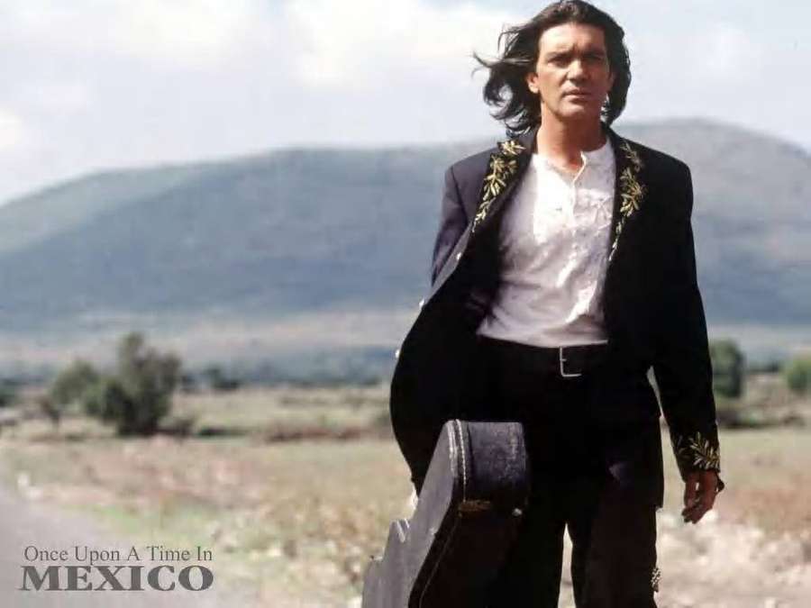 Man with long hair carrying guitar case in open field with hills — Once Background