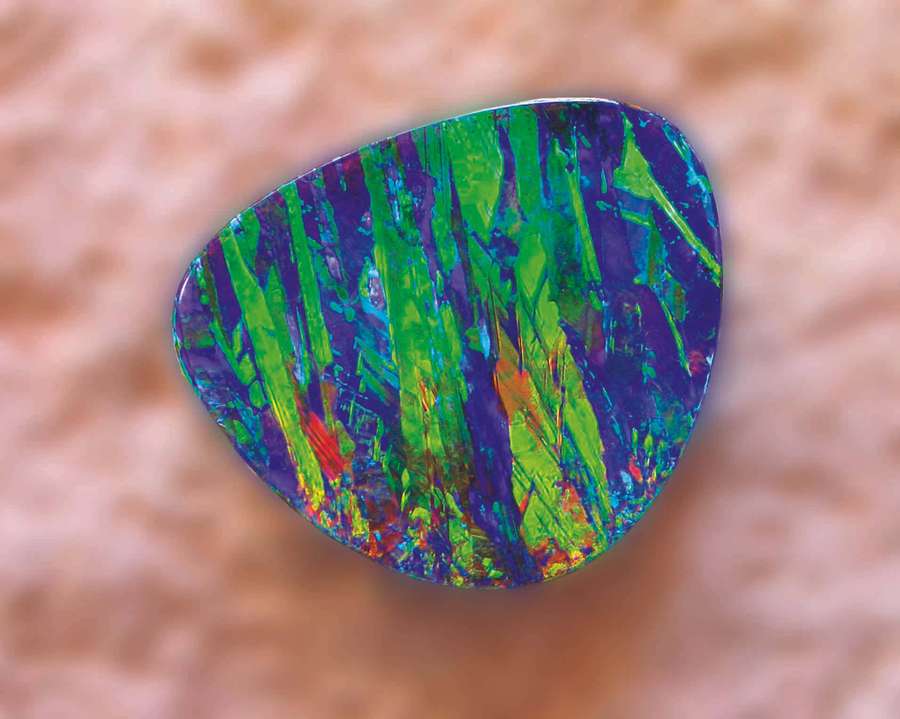 A colorful opal gemstone with green blue and purple hues on a peach background. — Opal Background
