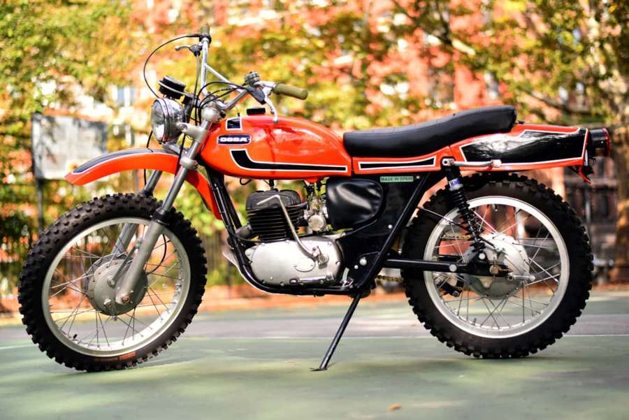 Vintage orange and black Ossa dirt bike parked on a green court. — Ossa Motorcycle Wallpaper