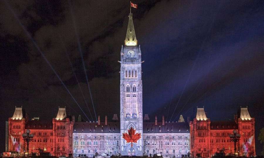 Kanadisches Parlamentsgebäude nachts mit roten Lichtern und einer Ahornblattprojektion beleuchtet. — Ottawa Wallpaper