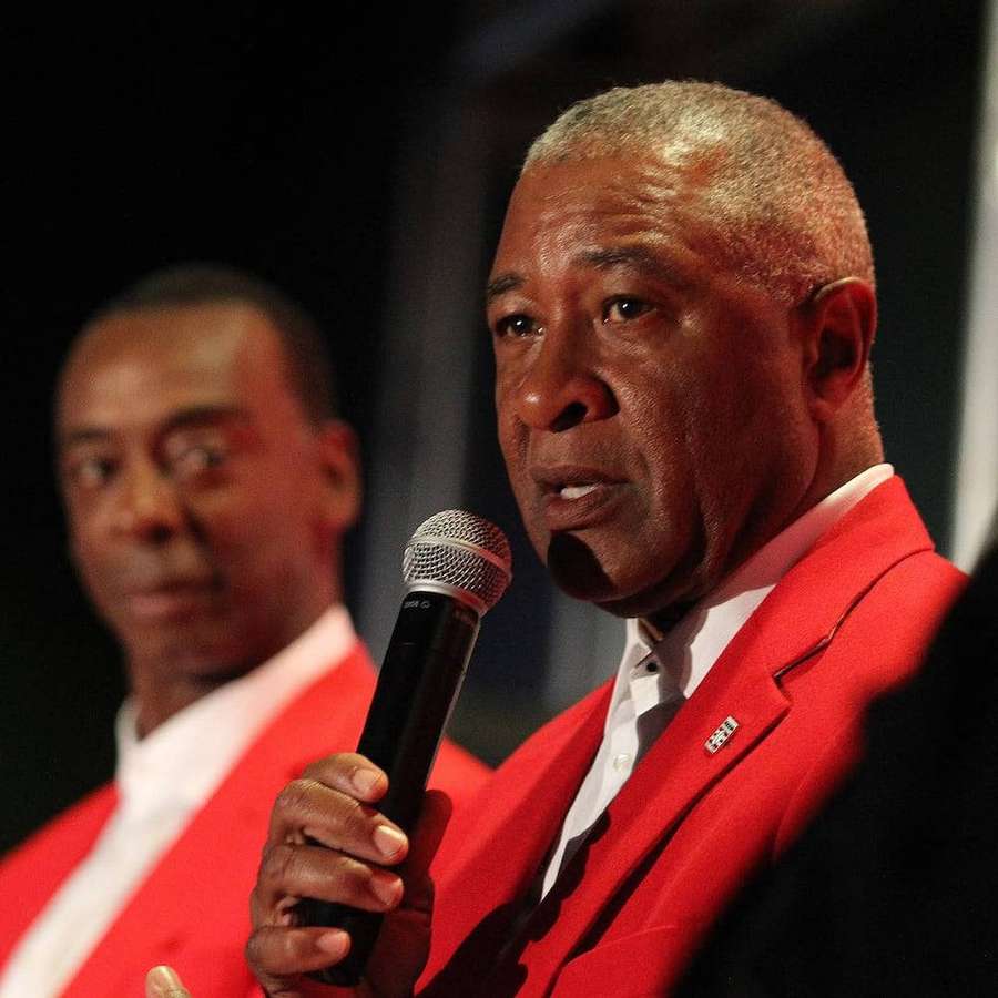 Two men in red suits one speaking into a microphone on stage. — Ozzie Smith Background