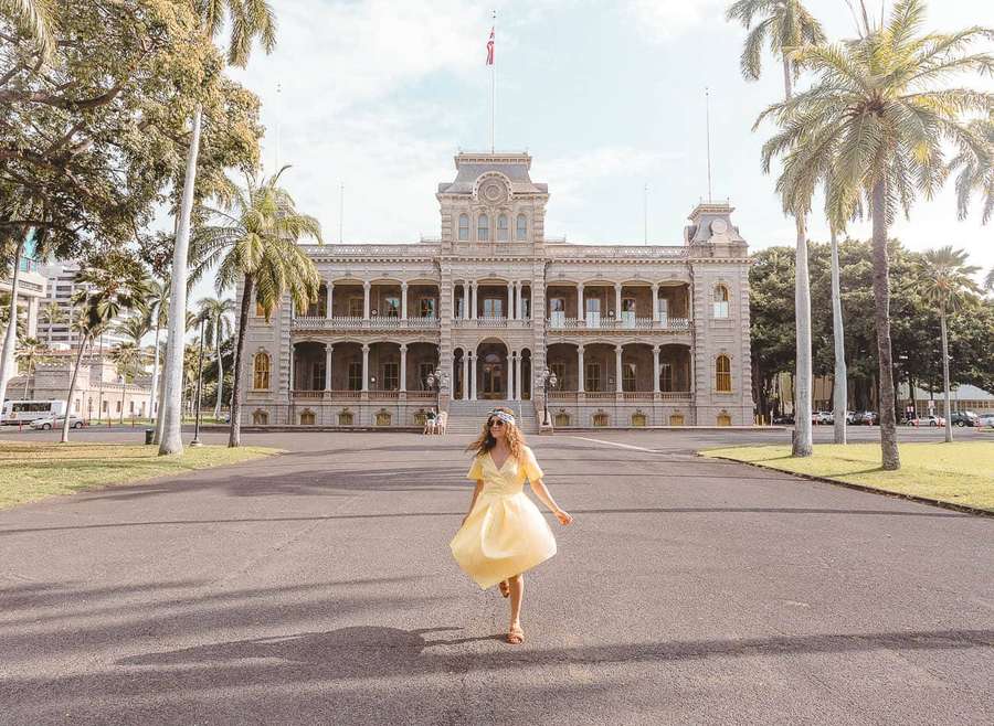 Mulher de vestido amarelo girando em frente a palácio histórico com palmeiras — Palácio Iolani Papéis de Parede