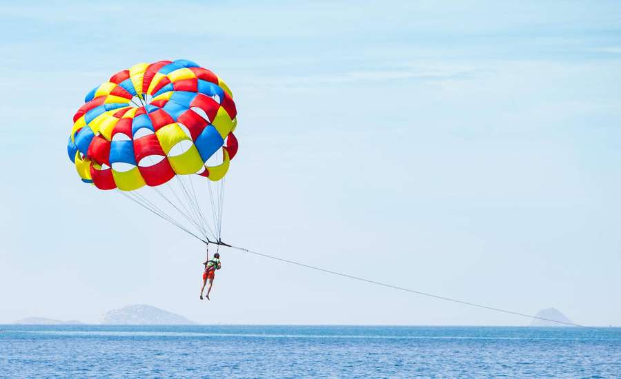 Person beim Parasailing über blauem Ozean mit buntem Fallschirm — Paragleiten Wallpaper