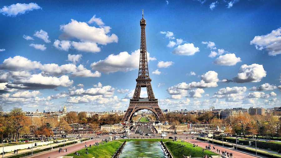 Eiffel Tower under a bright blue sky with scattered clouds and autumn trees. — Paris Background