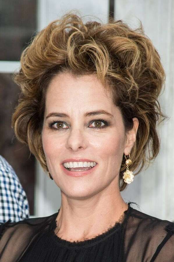 Uma mulher sorridente com cabelo cacheado e brincos de ouro em uma blusa preta transparente. — Parker Posey Papéis de Parede