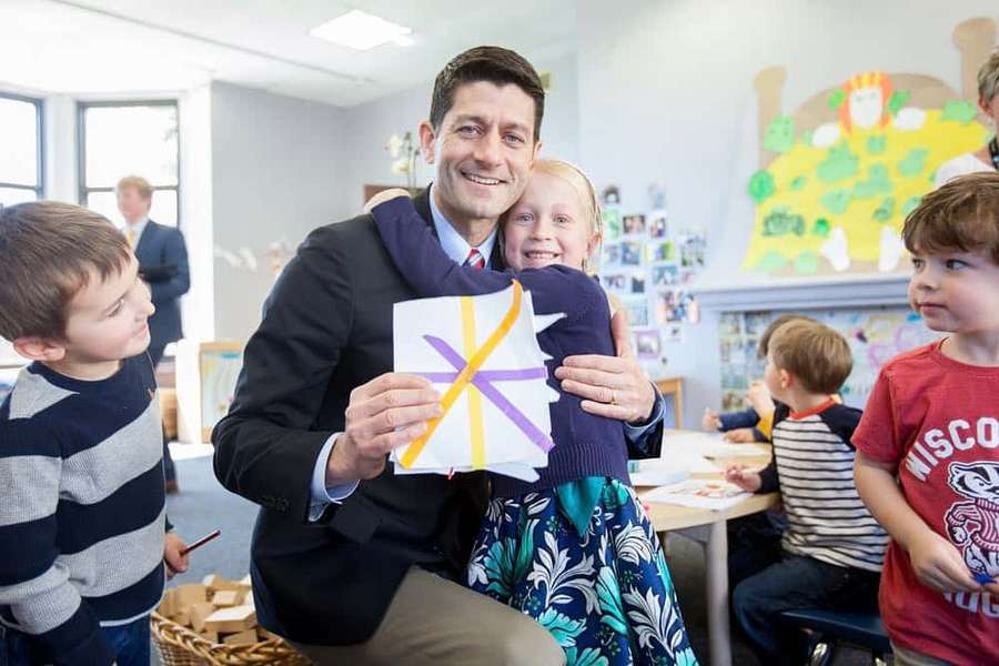 Man in suit holding child with paper craft in classroom with other children. — Paul Ryan Wallpaper