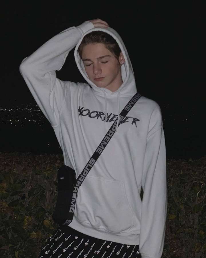 Giovane persona con felpa bianca con scritta 'MOORWATER' di notte con luci della città sullo sfondo. — Payton Sfondi
