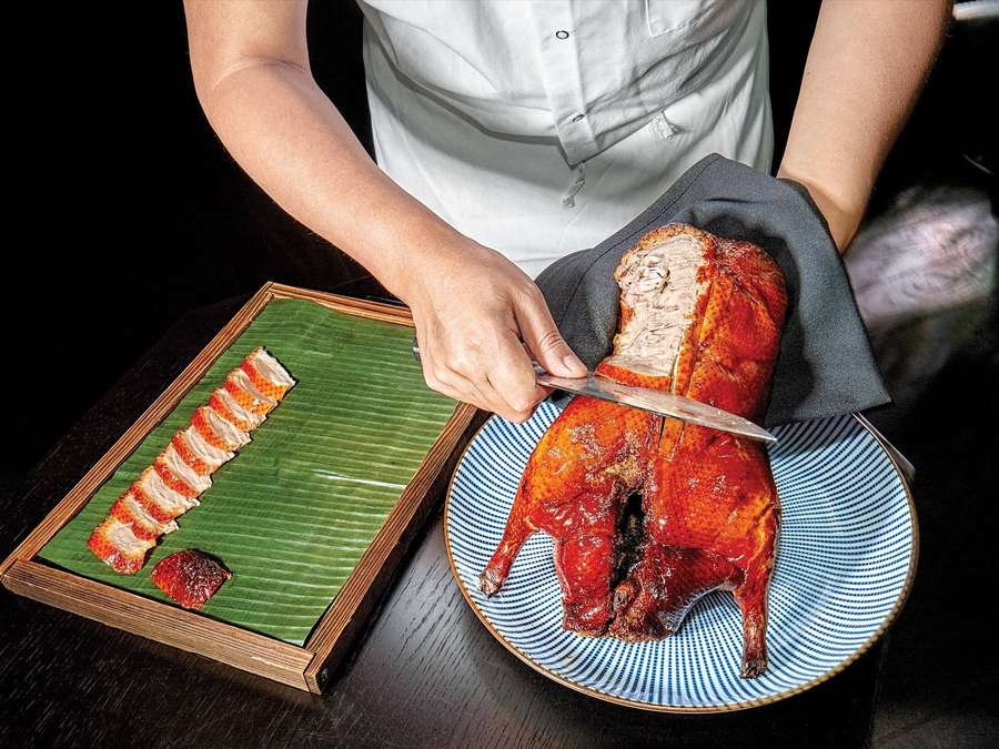 Chef slicing roasted duck with glossy skin on a blue plate beside banana leaf slices. — Peking Duck Wallpaper