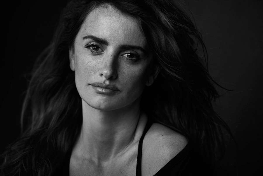 Close-up black and white portrait of a woman with windblown hair looking directly at viewer. — Penelope Wallpaper