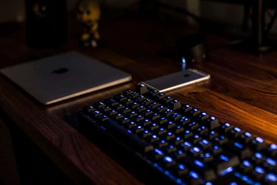 Teclado azul brillante sobre escritorio de madera con computadora portátil y teléfono en poca luz. — Periférico Fondos de pantalla