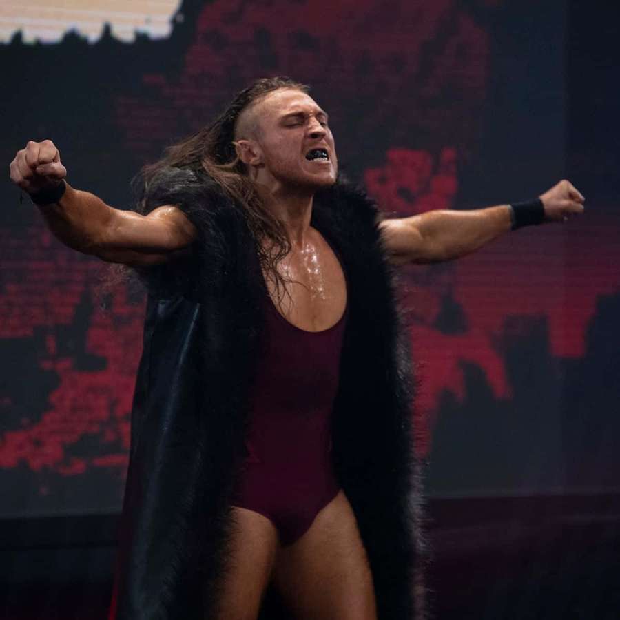 Wrestler in weinrotem Bodysuit und schwarzem Fellumhang feiert Sieg auf der Bühne. — Pete dunne Wallpaper