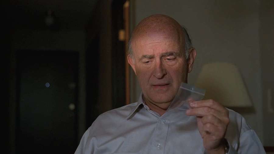 An older bald man holds a small plastic bag in a dimly lit room. — Peter Boyle Wallpaper