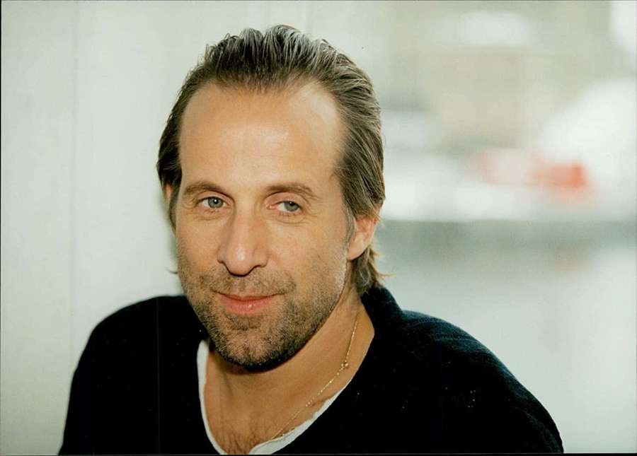 Man with gray hair and beard wearing black sweater and gold necklace — Peter Stormare Wallpaper