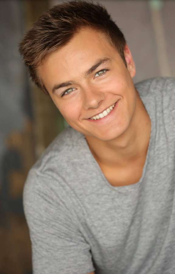 Young man smiling warmly in a gray t-shirt indoors — Peyton Background