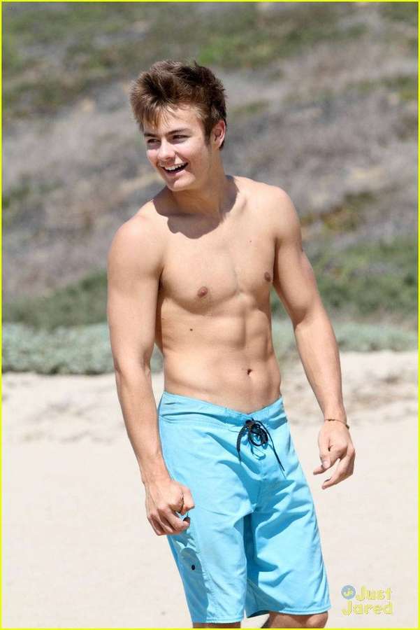 Young man laughing on sunny beach wearing blue swim trunks — Peyton Picture