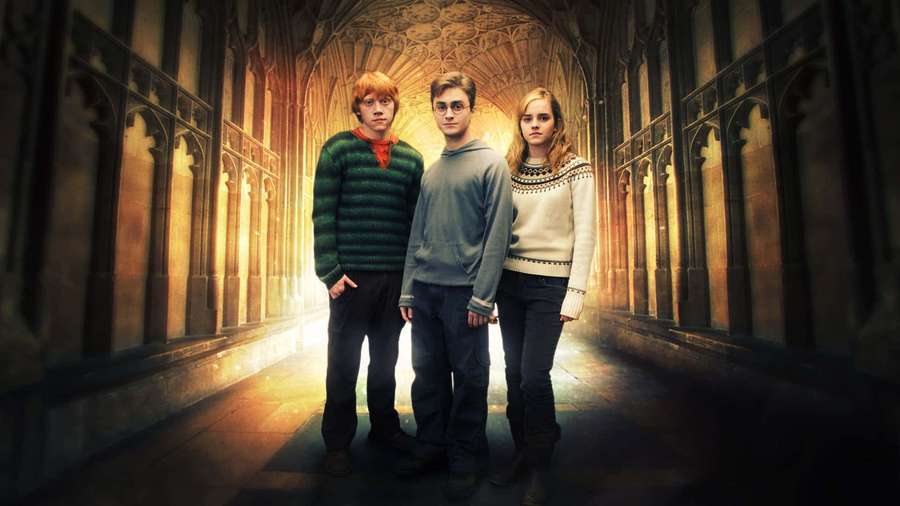 Three Harry Potter characters standing in a gothic school corridor with golden backlighting. — Phoenix Ikki Wallpaper