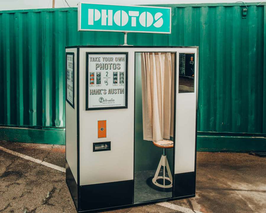 Eine vintage Fotokabine mit beigem Vorhang und orangefarbenem Knopf vor einer grünen Metallwand. — Photobooth Bilder