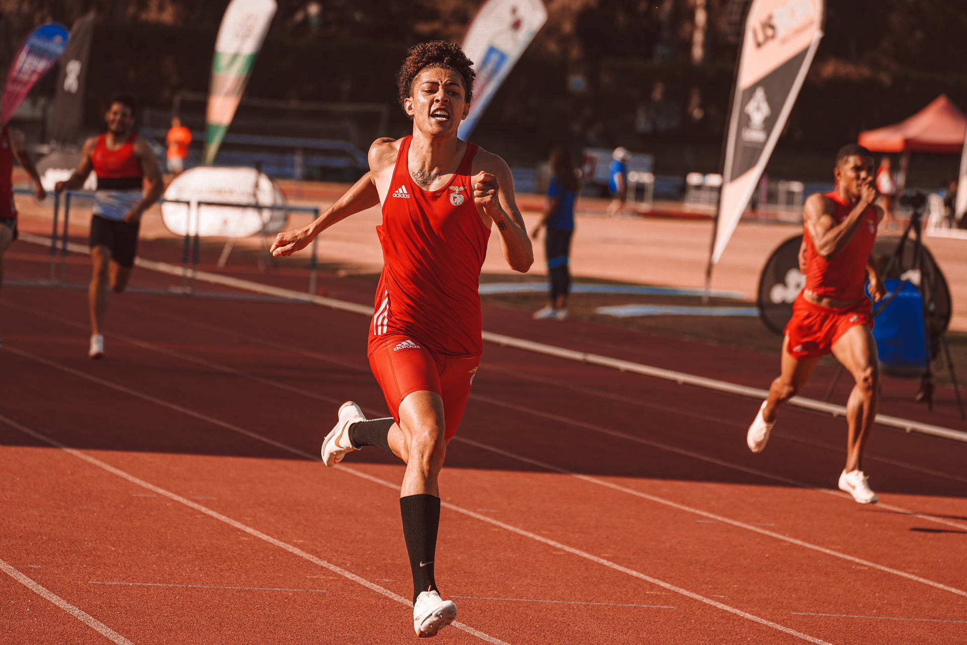 Ung manlig sprinter i röd uniform korsar mållinjen på bana — Fysisk bakgrund Bakgrundsbilder