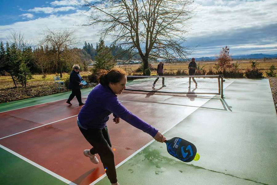 Menschen spielen Pickleball auf einem Außenplatz mit Bäumen und Hügeln im Hintergrund. — Pickleball Bild Bilder