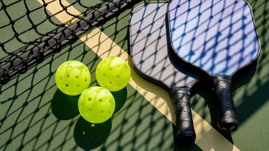 Pickleball paddles and balls on a court with net shadows from bright sun. — Pickleball Wallpaper