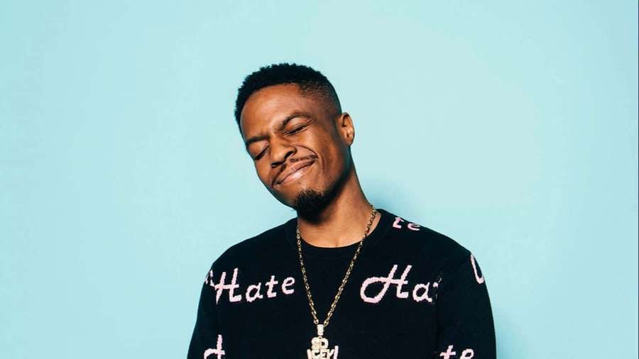 Man in black sweater with pink text smiling with eyes closed against blue background. — Pierre Bourne Wallpaper