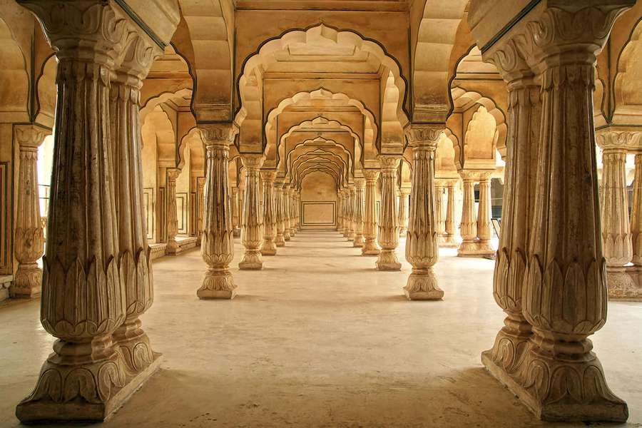 Grand stone corridor with repeating arches and pillars in a historic Indian building. — Pillar Background