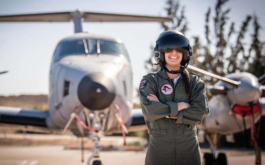 Female pilot in flight gear smiling with arms crossed in front of aircraft on tarmac. — Pilot Picture