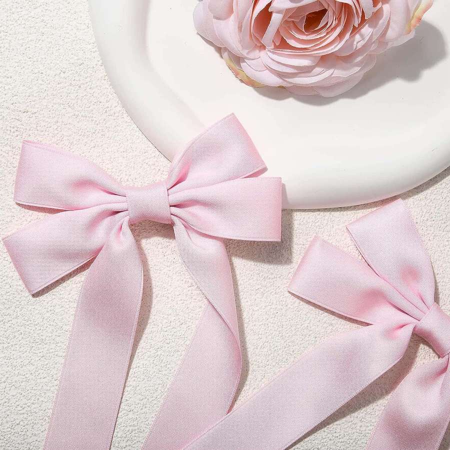 Two pink satin bows and a pink rose on a white textured surface. — Pink Bow Aesthetic Wallpaper
