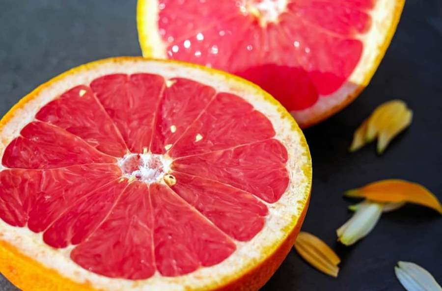 Sliced grapefruit with pink flesh and scattered petals on dark slate. — Pink Grapefruit Wallpaper