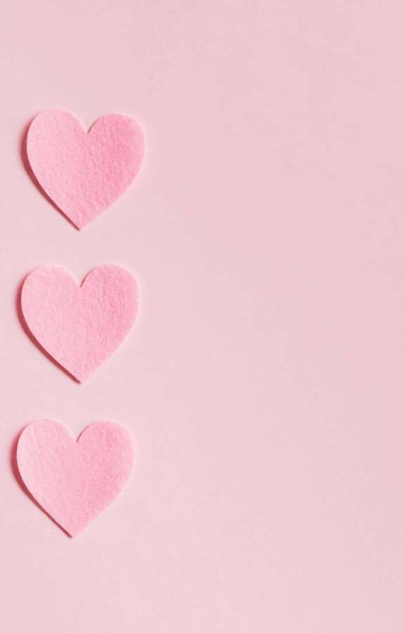 Three pink felt hearts aligned vertically on a pink surface. — Pink Hearts Background