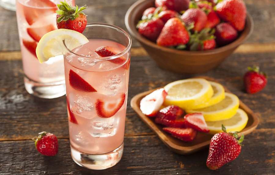 Two glasses of strawberry lemonade with ice and garnishes on a wooden table. — Pink Lemonade Wallpaper
