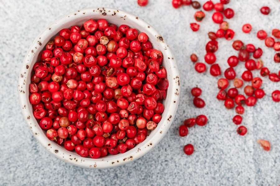 A bowl of red peppercorns with scattered berries on a gray surface. — Pink Peppercorn Wallpaper