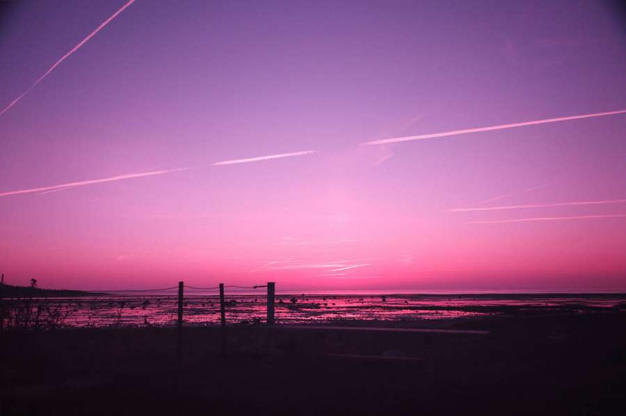 Vaaleanpunainen ja violetti auringonlasku veden yllä aitasiluetteineen — Pink Sunset Taustakuvat