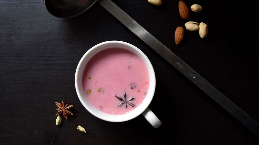 Pink spiced drink in white cup with star anise and pistachios on dark wood table. — Pink Tea Wallpaper