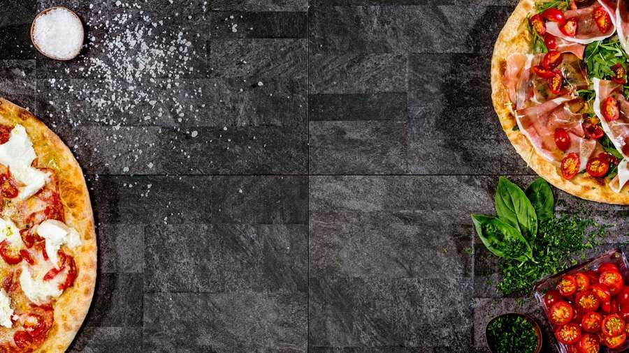 Two gourmet pizzas with toppings on a dark slate surface with fresh herbs and tomatoes. — Pizza Tower Background