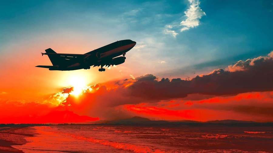 Airplane flying low over ocean at sunset with fiery orange sky. — Plane Background