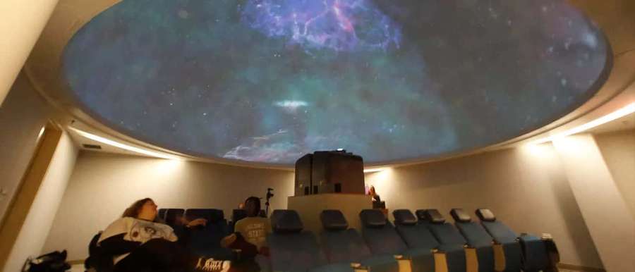 Personas sentadas en un planetario viendo una proyección de nebulosa estelar en el techo abovedado. — Planetario Fondos de pantalla