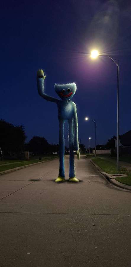Blue furry cartoon creature waving on a dark suburban street at night. — Playtime Wallpaper