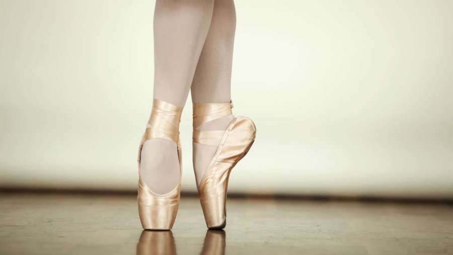 Ballerina's feet in gold pointe shoes standing on tiptoe on wooden floor. — Pointe Shoes Wallpaper