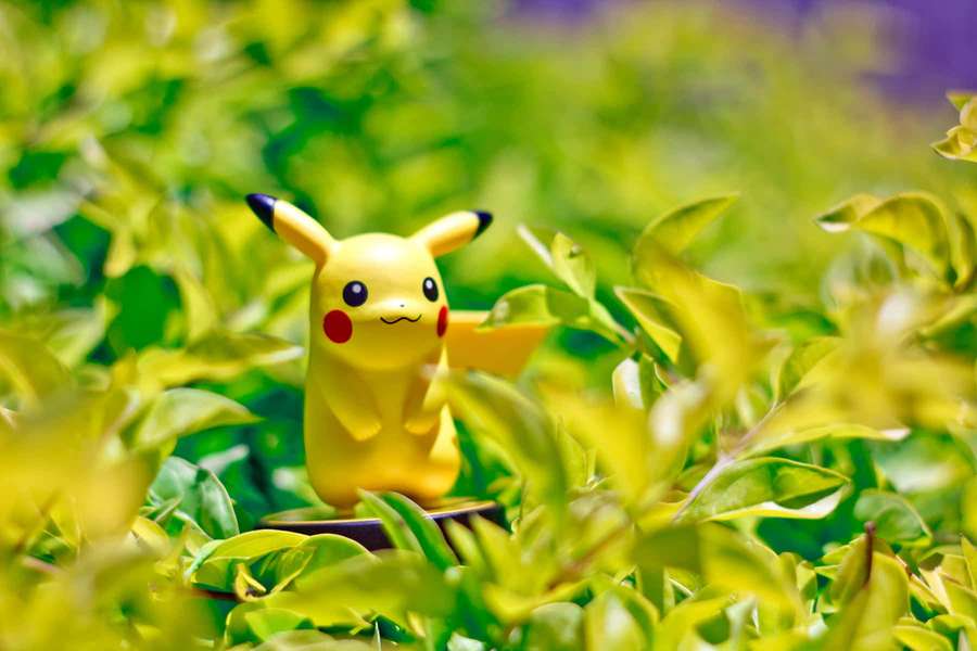 Gelbe Pikachu-Spielfigur umgeben von grünen Blättern im Sonnenlicht. — Pokemon Figures Wallpaper