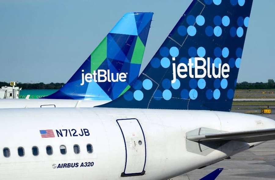 Two JetBlue airplanes parked on airport tarmac showing their colorful tails. — Polka Background