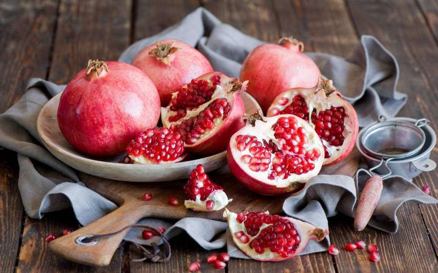 Fresh pomegranates with seeds scattered on a wooden table with gray cloth. — Pomegranate Wallpaper