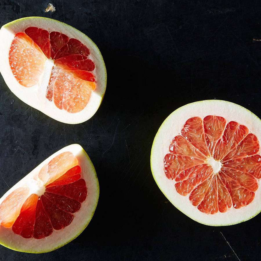 Tres mitades de pomelo cortadas sobre una superficie oscura que muestran segmentos jugosos. — Pomelo Fondos de pantalla