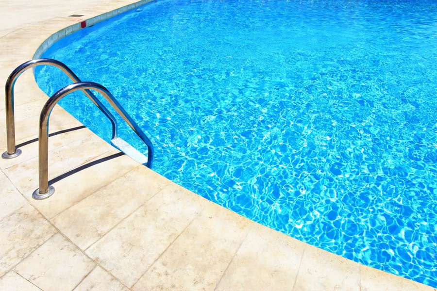 Clear blue swimming pool with metal ladder on stone deck under bright sun. — Pool Background