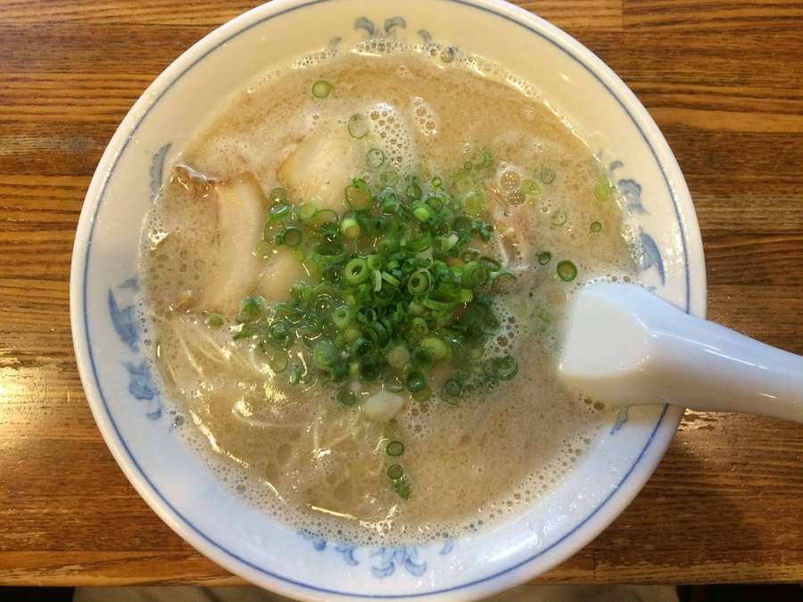 A bowl of ramen with green onions and a spoon on a wooden table. — Porky Background