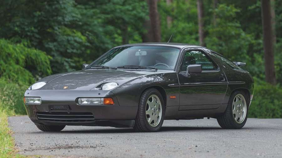 Dark gray Porsche 928 sports car parked on gravel road in forest. — Porsche 928 Wallpaper